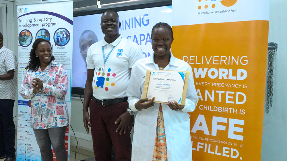 Andezo Moureen (R) receiving her certificate of achievement from UNFPA Programme Analyst Roy Asiku (C). 