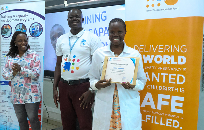 Andezo Moureen (R) receiving her certificate of achievement from UNFPA Programme Analyst Roy Asiku (C). 